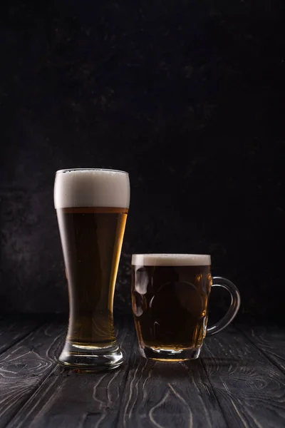 Glas und Becher mit frischem Leichtbier mit Schaumstoff auf Holztisch — Stockfoto