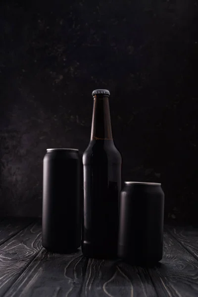 Bouteille entre boîtes métalliques noires de bière sur table en bois — Photo de stock