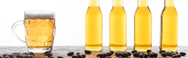 Panoramic shot of bottles and mug of light beer near coffee beans isolated on white — Stock Photo