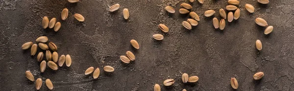 Panoramic shot of scattered pistachios on brown textured surface — Stock Photo
