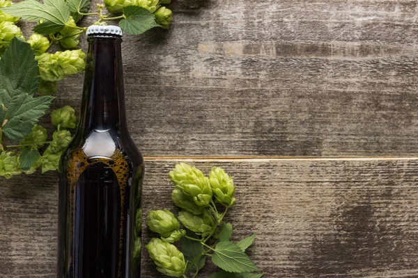 Вид сверху на свежее пиво в бутылке с зеленым хмелем на деревянном фоне — стоковое фото