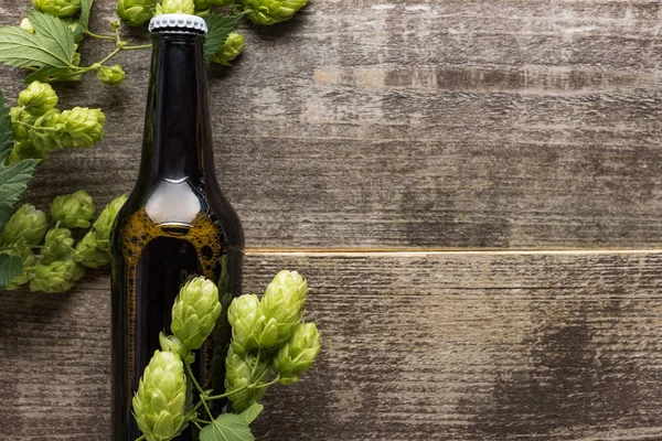 Top view of beer in brown bottle with green hop on wooden surface — Stock Photo
