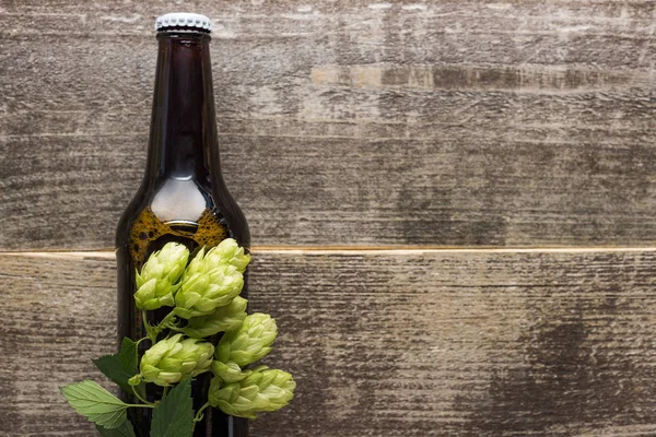 Vista superior de la cerveza fresca en botella con lúpulo verde sobre superficie de madera - foto de stock