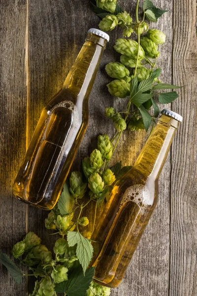 Vista superior de la cerveza en botellas con lúpulo verde en mesa de madera - foto de stock