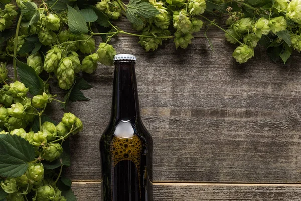 Vista superior de la cerveza en botella marrón con lúpulo verde en mesa rústica de madera - foto de stock