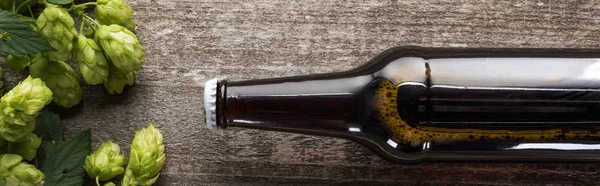 Top view of beer in brown bottle with green hop on wooden background, panoramic shot — Stock Photo