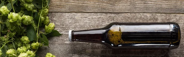 Vista dall'alto di birra in bottiglia vicino hop su sfondo di legno, colpo panoramico — Foto stock