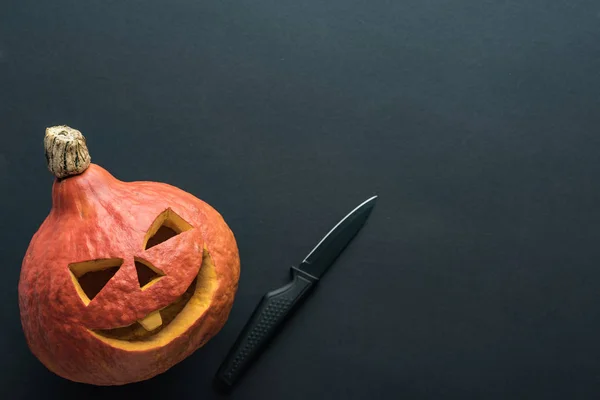 Vista superior de la espeluznante calabaza de Halloween con cuchillo sobre fondo negro - foto de stock