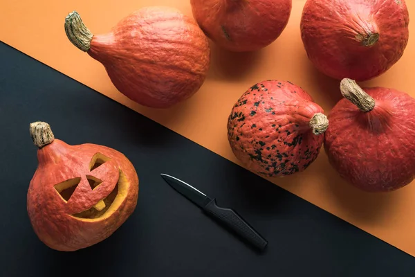 Vista superior de calabazas de Halloween con cuchillo sobre fondo naranja y negro - foto de stock