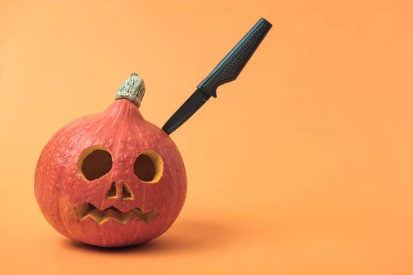 Calabaza de Halloween con cuchillo sobre fondo naranja - foto de stock
