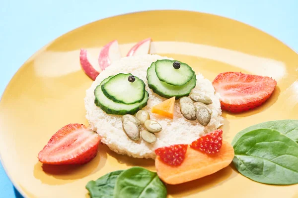 Закрытый вид на тарелку с причудливым лицом из еды для детского завтрака на голубом фоне — стоковое фото
