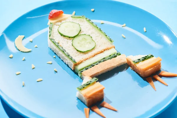 Vista de cerca de la placa con cohete hecho de comida para niños desayuno sobre fondo azul - foto de stock