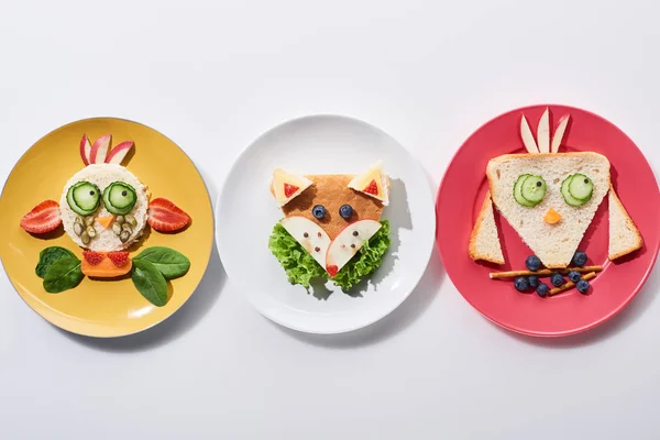 Vista dall'alto di piatti con mucca fantasia, uccello e volpe fatti di cibo per la colazione dei bambini su sfondo bianco — Foto stock