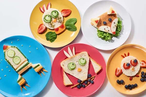 Top view plaques pf avec des animaux de fantaisie et fusée faite de nourriture pour le petit déjeuner des enfants sur fond blanc — Photo de stock