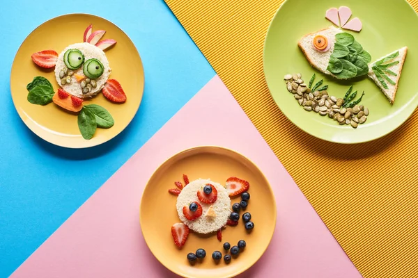 Vue de dessus des assiettes avec des animaux de fantaisie faits de nourriture sur fond bleu, jaune et rose — Photo de stock