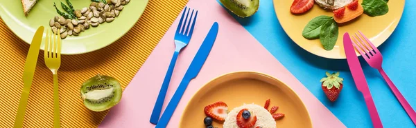 Top view of plates with fancy animals made of food for childrens breakfast on blue, yellow and pink background with colorful cutlery — Stock Photo