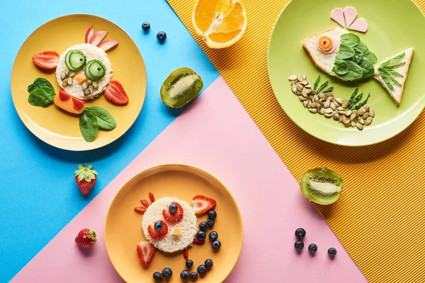 Top view of plates with fancy animals made of food for childrens breakfast on blue, yellow and pink background — Stock Photo