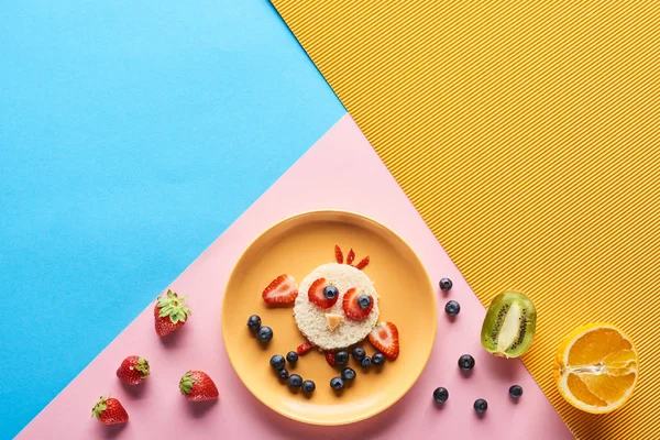 Вид зверху на тарілку з вишуканими тваринами з їжі для дитячого сніданку на синьому, жовтому та рожевому тлі — стокове фото