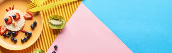 Верхний вид на тарелку с модным животным из продуктов питания для детей завтрак возле столовых приборов на голубом, желтом и розовом фоне — стоковое фото