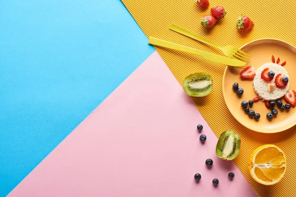 Vista superior da placa com animal de fantasia feito de alimentos para crianças café da manhã perto de talheres em fundo azul, amarelo e rosa — Fotografia de Stock