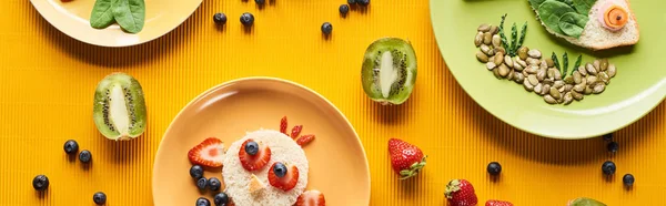 Vue de dessus des assiettes avec des animaux de fantaisie faits de nourriture sur fond orange coloré, vue panoramique — Photo de stock