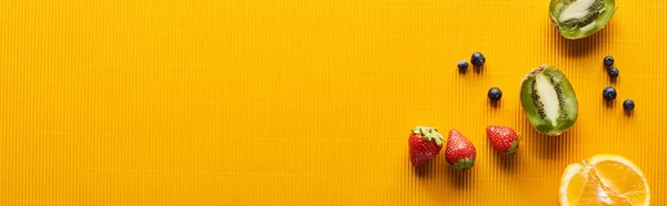 Top view of strawberry, blueberry, kiwi and orange on colorful orange background, panoramic shot — Stock Photo