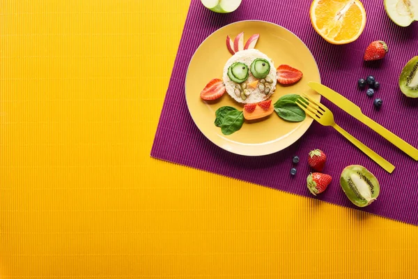 Vista dall'alto del piatto con mucca fantasia fatta di cibo con posate su sfondo viola e arancione — Foto stock