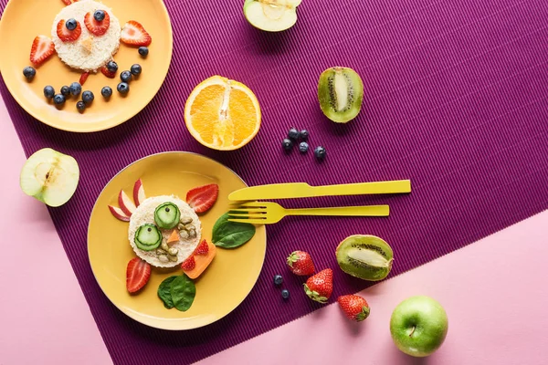 Vista superior de platos con animales de lujo hechos de comida cerca de frutas sobre fondo púrpura - foto de stock