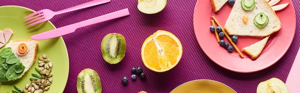 Vista superior de platos con animales de lujo hechos de alimentos cerca de frutas sobre fondo púrpura, plano panorámico - foto de stock