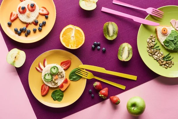 Vista dall'alto di piatti con animali fantasia fatti di cibo vicino a frutta su sfondo viola — Foto stock