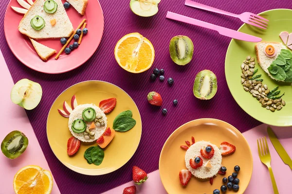 Top view of plates with fancy animals made of food near fruits on purple background — Stock Photo