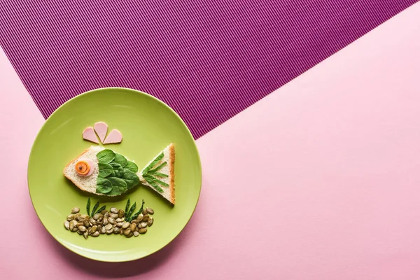 Vista dall'alto del piatto con pesce fantasia fatto di cibo su sfondo rosa e viola — Foto stock