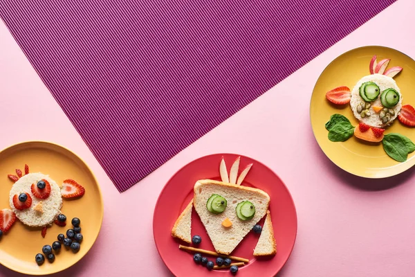 Vista superior de platos con animales de lujo hechos de comida sobre fondo rosa y púrpura - foto de stock