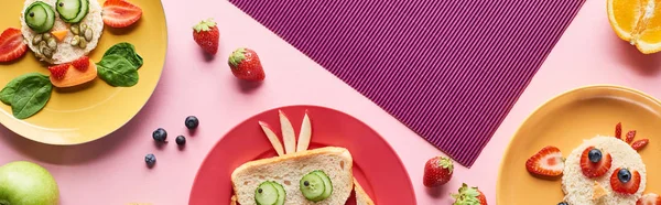 Vue de dessus des assiettes avec des animaux de fantaisie faits de nourriture sur fond rose et violet avec des fruits, vue panoramique — Photo de stock