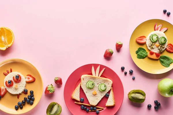 Vue de dessus des assiettes avec des animaux de fantaisie faits de nourriture sur fond rose avec des fruits — Photo de stock