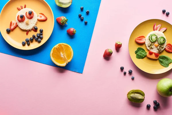 Vista superior de pratos com animais extravagantes feitos de comida em fundo azul e rosa com frutas — Fotografia de Stock