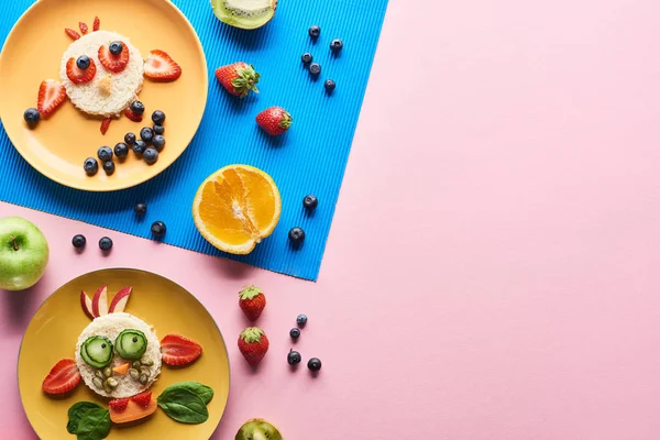 Vista dall'alto di piatti con animali di fantasia fatti di cibo su sfondo blu e rosa con frutta — Foto stock