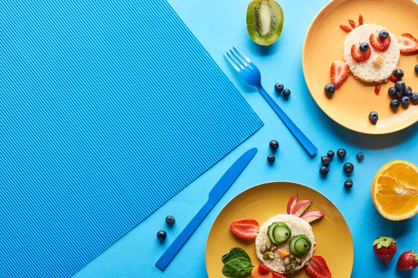 Vista superior de platos con animales de lujo hechos de comida sobre fondo azul - foto de stock