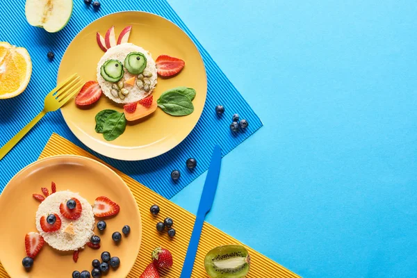 Vista superior de placas com animais extravagantes feitos de comida em fundo azul e amarelo — Fotografia de Stock