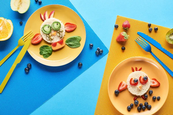 Vista superior de placas com animais extravagantes feitos de comida em fundo azul e amarelo — Fotografia de Stock