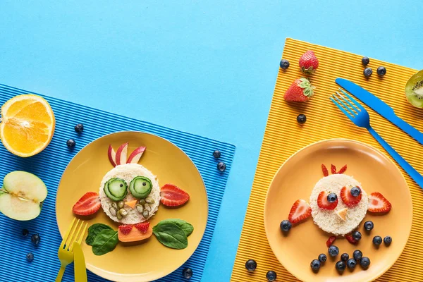 Vista superior de placas com animais extravagantes feitos de comida em fundo azul e amarelo — Fotografia de Stock