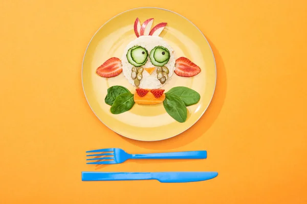 Top view of plate with fancy cow made of food for childrens breakfast near cutlery on orange background — Stock Photo