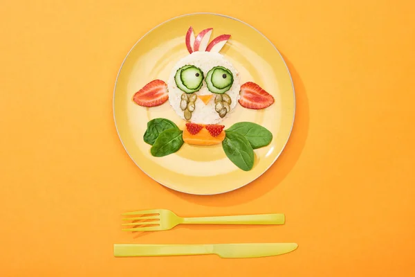 Vue du dessus de l'assiette avec vache de fantaisie faite de nourriture pour le petit déjeuner des enfants près de couverts sur fond orange — Photo de stock