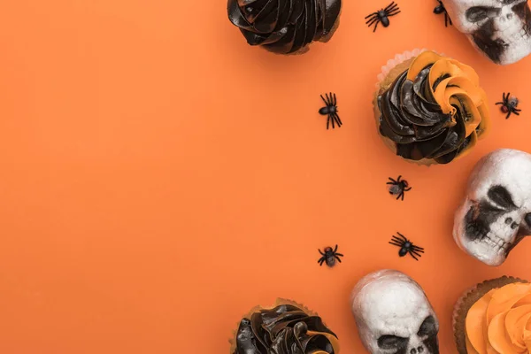 Draufsicht auf köstliche Halloween-Cupcakes mit Spinnen und Totenköpfen auf orangefarbenem Hintergrund mit Kopierraum — Stockfoto