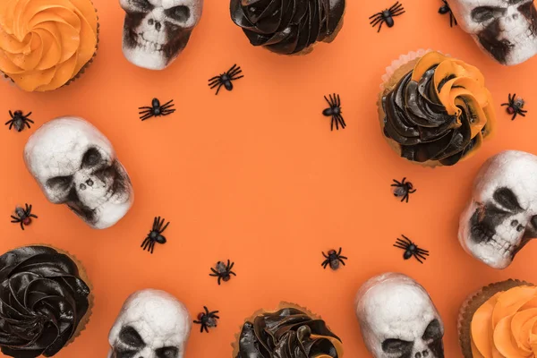 Draufsicht auf köstliche Halloween-Cupcakes mit Spinnen und Totenköpfen auf orangefarbenem Hintergrund mit Kopierraum — Stockfoto