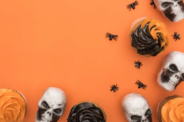 Vista superior de cupcakes de Halloween con arañas y calaveras sobre fondo naranja con espacio para copiar - foto de stock