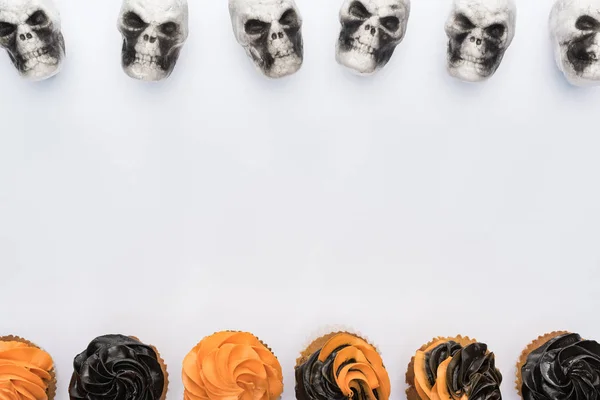 Vista superior de deliciosos cupcakes y calaveras de Halloween sobre fondo blanco con espacio para copiar - foto de stock