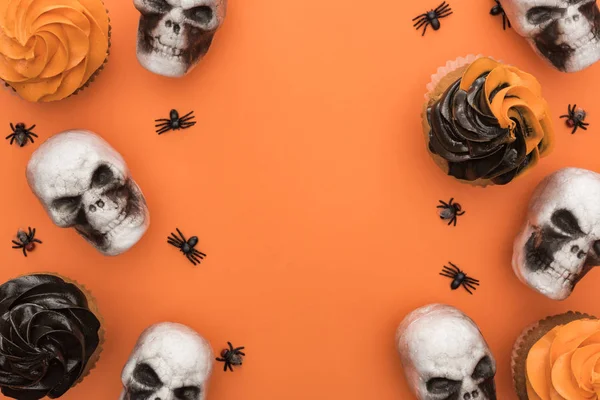 Vista superior de sabrosos cupcakes de Halloween con arañas y calaveras sobre fondo naranja con espacio de copia - foto de stock