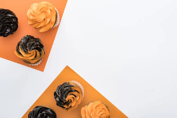 Vue du dessus de délicieux cupcakes d'Halloween sur fond orange et blanc avec espace de copie — Photo de stock