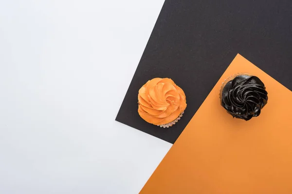 Draufsicht auf köstliche Halloween-Cupcakes auf schwarzem, orangefarbenem und weißem Hintergrund mit Kopierfläche — Stockfoto
